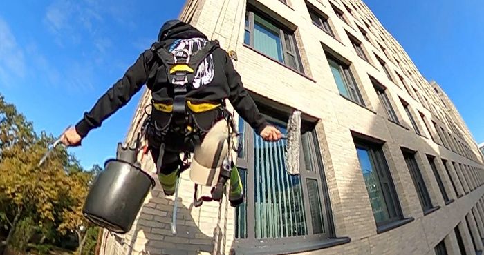Ein Mitarbeiter hängt am Seil, um die Fenster zu putzen